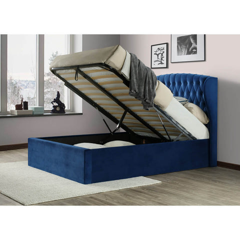 Warwick blue velvet wingback ottoman bed with mattress base lifted open showing under-bed storage in a styled bedroom